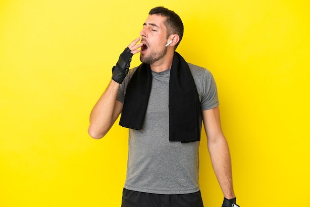 Homem caucasiano esportivo jovem isolado em fundo amarelo bocejando e cobrindo a boca aberta com a mão