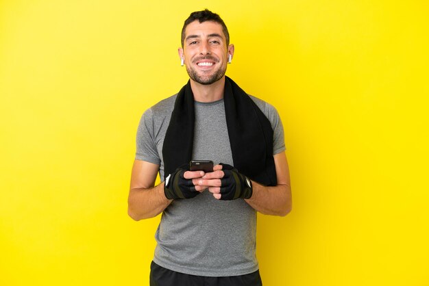 Homem caucasiano esportivo jovem isolado em fundo amarelo enviando uma mensagem com o celular