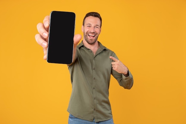 Homem caucasiano excitado segurando um celular em branco mostrando a tela para a câmera apontando para ele recomendando