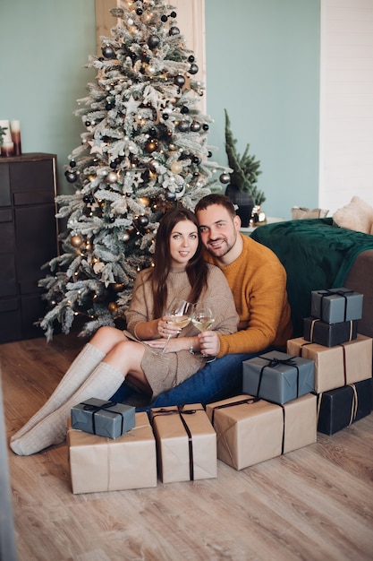 Homem caucasiano forte decora a árvore de natal com sua linda namorada com presentes de ano novo