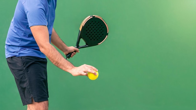Homem caucasiano jogando uma partida aberta com raquete de padel preta e bola amarela