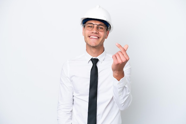 Homem caucasiano jovem arquiteto com capacete e segurando plantas isoladas no fundo branco, fazendo gesto de dinheiro