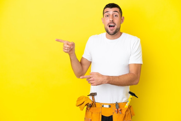 Homem caucasiano jovem eletricista isolado em fundo amarelo surpreso e apontando o lado