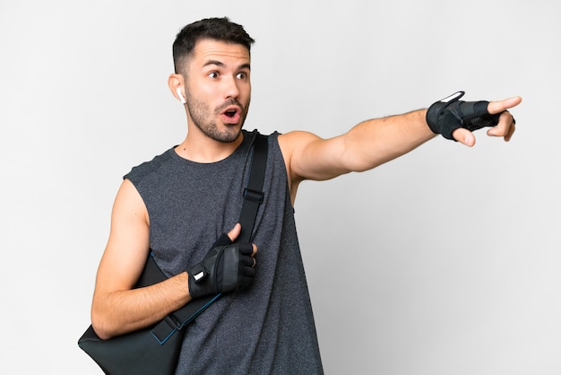 Foto homem caucasiano jovem esporte com bolsa esportiva sobre fundo branco isolado apontando para fora