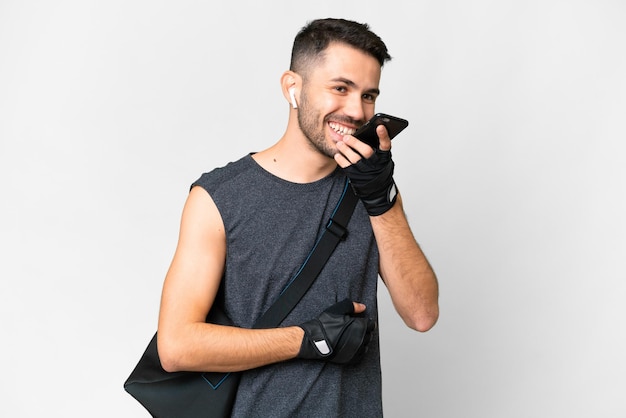 Homem caucasiano jovem esporte com bolsa esportiva sobre fundo branco isolado, mantendo uma conversa com o telefone celular com alguém