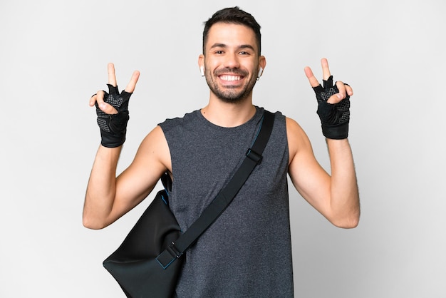 Homem caucasiano jovem esporte com bolsa esportiva sobre fundo branco isolado, mostrando sinal de vitória com as duas mãos