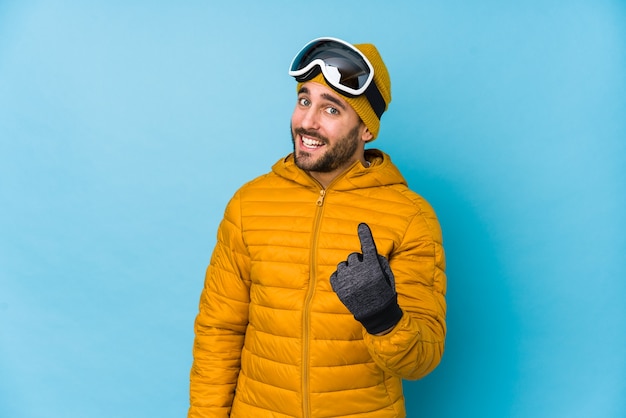 Homem caucasiano jovem esquiador isolado apontando com o dedo para você como se fosse um convite para se aproximar.