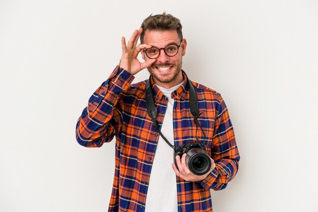 Homem caucasiano jovem fotografia isolado no fundo branco animado mantendo o gesto ok no olho.