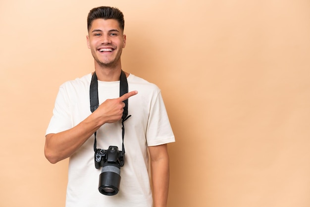 Homem caucasiano jovem fotógrafo isolado em fundo bege, apontando para o lado para apresentar um produto