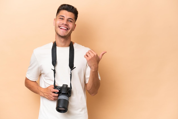 Homem caucasiano jovem fotógrafo isolado em fundo bege, apontando para o lado para apresentar um produto