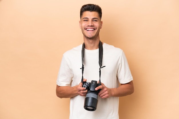 Homem caucasiano jovem fotógrafo isolado em fundo bege, mantendo os braços cruzados na posição frontal