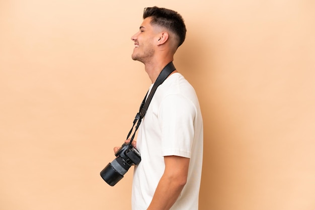 Homem caucasiano jovem fotógrafo isolado em fundo bege na posição lateral