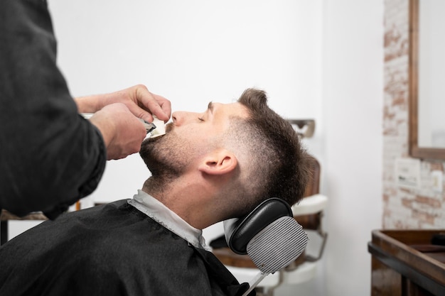 Homem caucasiano jovem hipster durante a preparação da barba na barbearia moderna Estilo de cabelo masculino Homem bonito, recebendo novo penteado com aparador elétrico Fotografia de alta qualidade