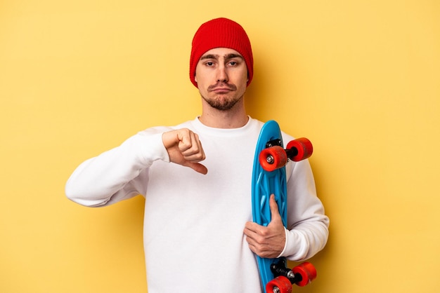 Homem caucasiano jovem patinador isolado em fundo amarelo, mostrando um gesto de desagrado, polegares para baixo. Conceito de desacordo.