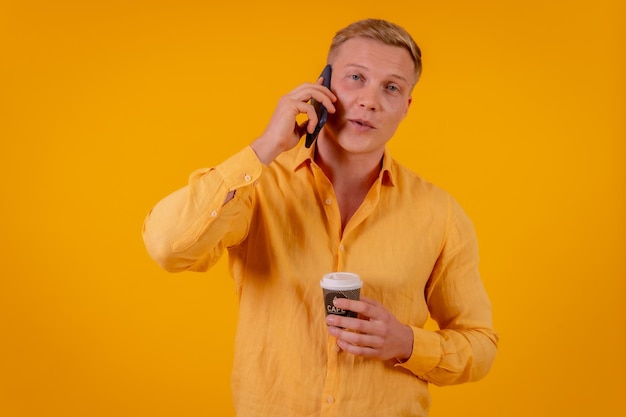 Homem caucasiano loiro em um fundo amarelo fazendo uma chamada com o telefone