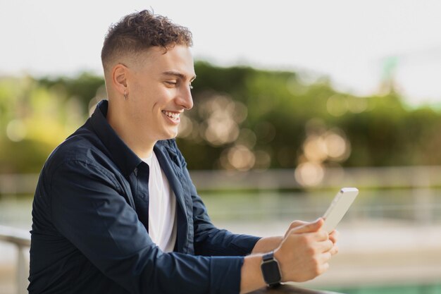 Homem caucasiano millennial feliz em digitação casual em telefone celular caminhando na cidade ao ar livre