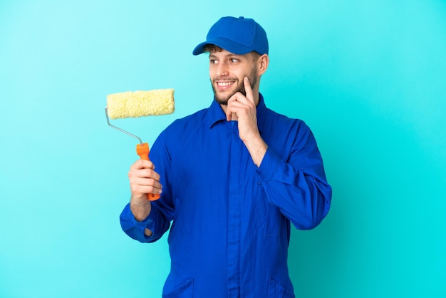 Homem caucasiano pintor isolado em fundo azul pensando em uma ideia enquanto olha para cima