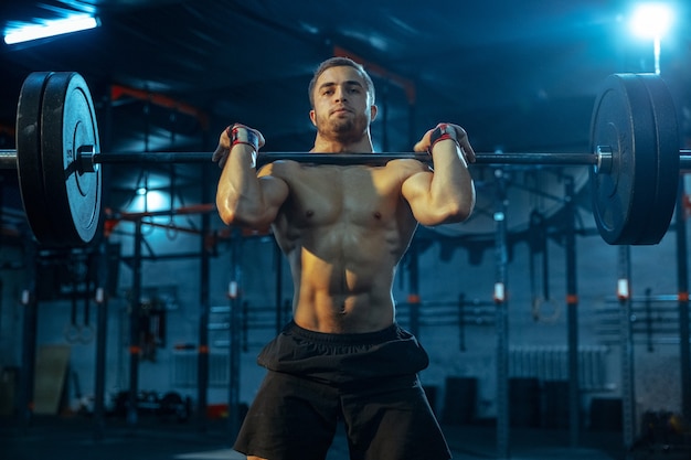 Homem caucasiano praticando levantamento de peso no ginásio. Modelo esportivo masculino caucasiano treinando com barra, parece confiante e forte. Musculação, estilo de vida saudável, movimento, atividade, conceito de ação.