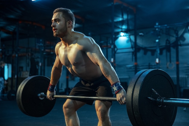 Homem caucasiano praticando levantamento de peso no ginásio. modelo esportivo masculino caucasiano treinando com barra, parece confiante e forte. musculação, estilo de vida saudável, movimento, atividade, conceito de ação.