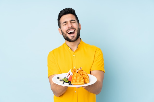 Homem caucasiano segurando waffles na parede azul