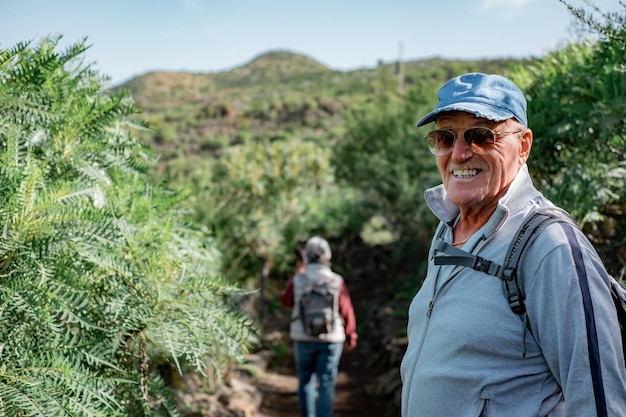 Homem caucasiano sênior feliz em excursão ao ar livre em sorrisos de montanha olhando para a câmera desfrutando de graça