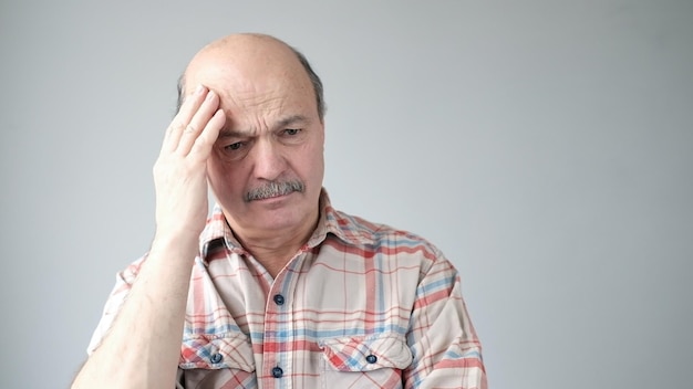 Homem caucasiano sênior mostrando o quanto sua cabeça dói sentindo dor