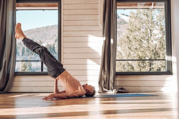Homem caucasiano sênior praticando yoga asana clássico em treinamento de estúdio em frente a uma janela