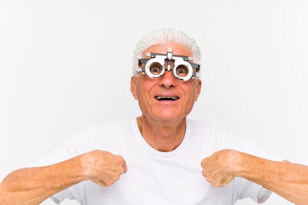Homem caucasiano sênior, vestindo um quadro de julgamento optometrista surpreendeu apontando para si mesmo, sorrindo amplamente.