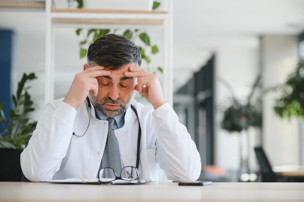 Homem caucasiano sênior vestindo uniforme médico e estetoscópio na clínica esfregando os olhos para fadiga e dor de cabeça sonolento e cansado problema de visão de expressão