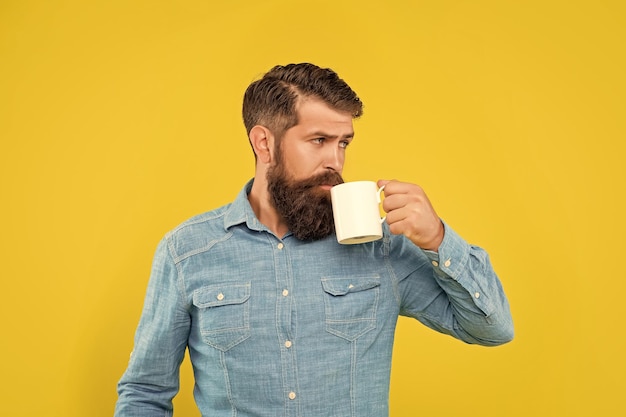 Homem caucasiano sério bebendo café de fundo amarelo de caneca