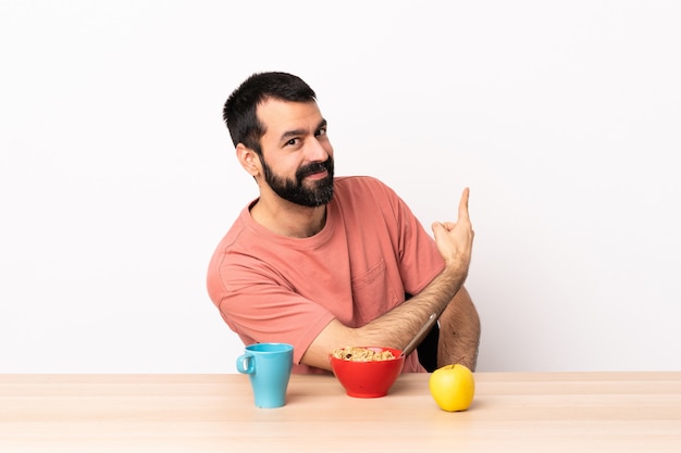 Homem caucasiano, tomando café da manhã em uma mesa apontando para trás