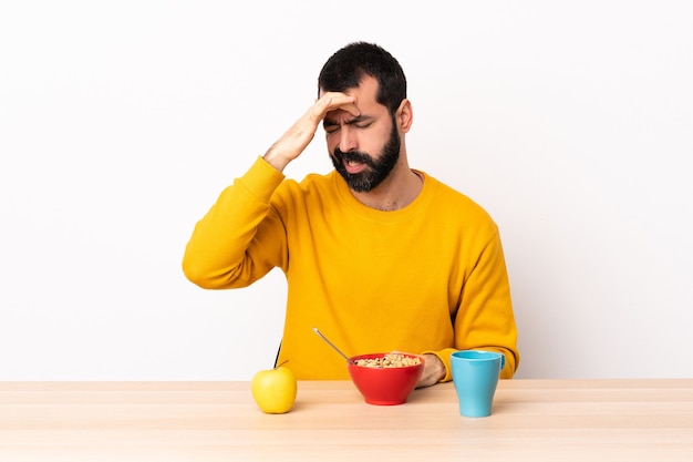 Homem caucasiano tomando café da manhã em uma mesa com dor de cabeça.