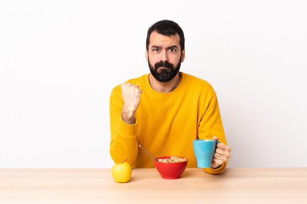 Homem caucasiano, tomando café da manhã em uma mesa com expressão infeliz