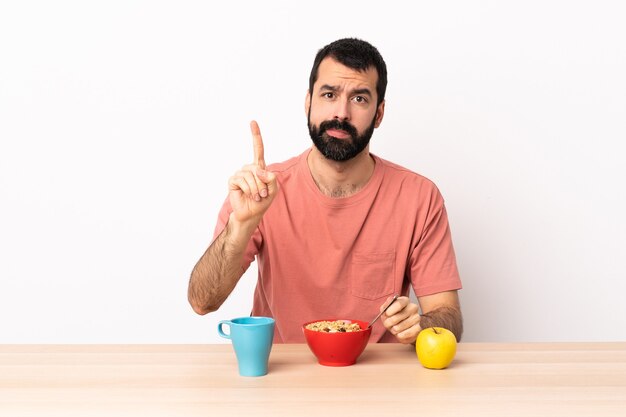 Homem caucasiano tomando café da manhã em uma mesa contando um com expressão séria.