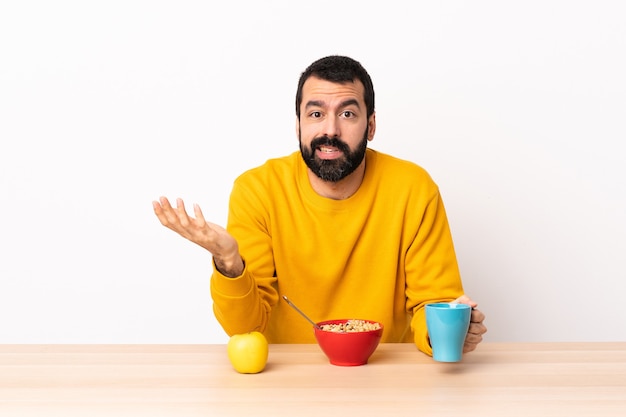 Homem caucasiano tomando café da manhã em uma mesa, fazendo gesto de dúvidas.