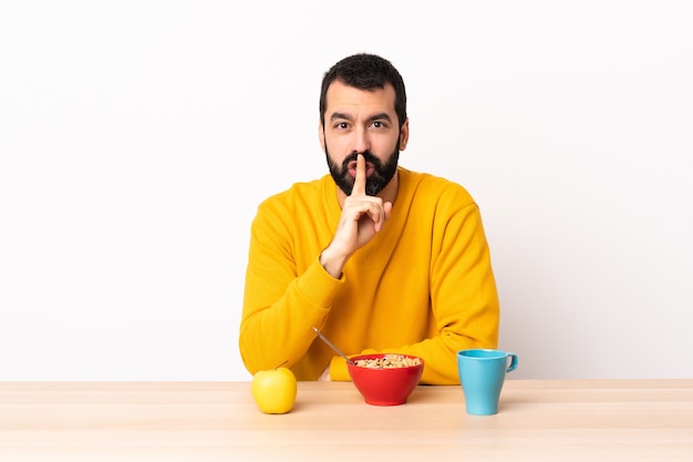 Homem caucasiano tomando café da manhã em uma mesa mostrando um sinal de silêncio gesto colocando o dedo na boca.