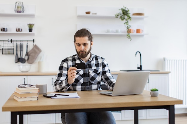 Homem caucasiano usando cartão de crédito enquanto usa computador portátil