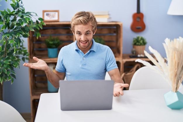 Homem caucasiano usando laptop fazendo videochamada comemorando conquista com sorriso feliz e expressão vencedora com a mão erguida