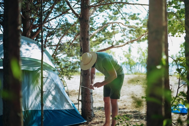 Homem caucasiano usando um chapéu colocando uma barraca Conceito de acampamento familiar