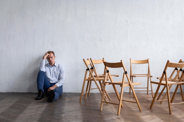 Foto homem chateado em sessão de terapia de grupo com cadeiras vazias