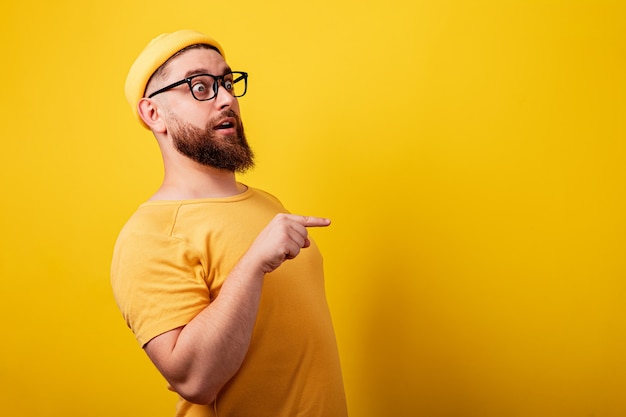 Homem chocado apontando para o espaço vazio do layout sobre fundo amarelo, conceito de publicidade