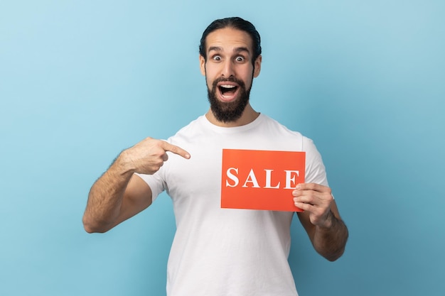 Homem chocado com barba vestindo camiseta branca apontando o dedo para o cartão de venda na mão