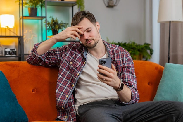 Homem chocado e triste usando smartphone lendo mensagem de e-mail negativa se sente irritado com o acidente do vírus do aplicativo