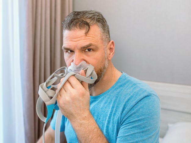 homem chocado infeliz com problemas respiratórios crônicos surpreso ao usar uma máquina de cpap sentado na cama