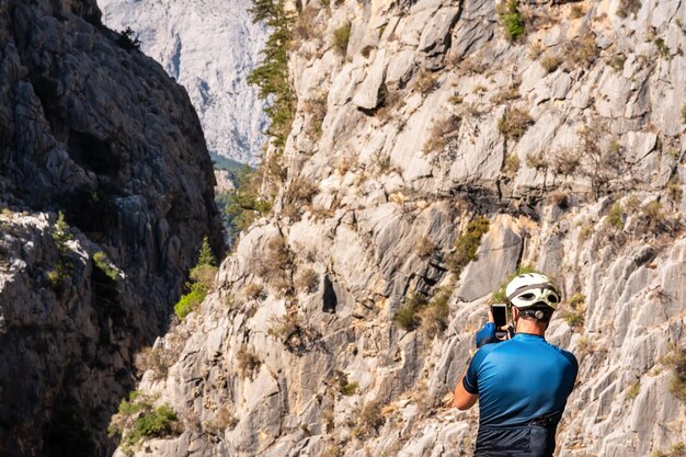 Homem ciclista com capacete fotografa uma paisagem montanhosa com um smartphone