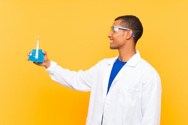 Homem científico segurando um balão de laboratório sobre parede isolada com expressão feliz