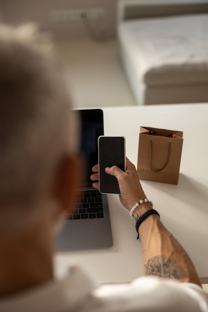 Homem clicando em seu smartphone perto de uma bolsa marrom