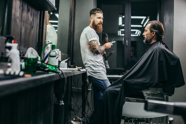 homem coberto com um vestido de cabeleireiro e conversando com seu barbeiro profissional