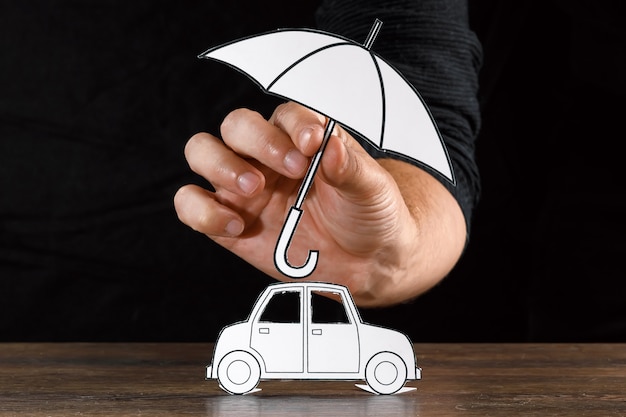 Homem cobre um carro de papel com guarda-chuva de papel