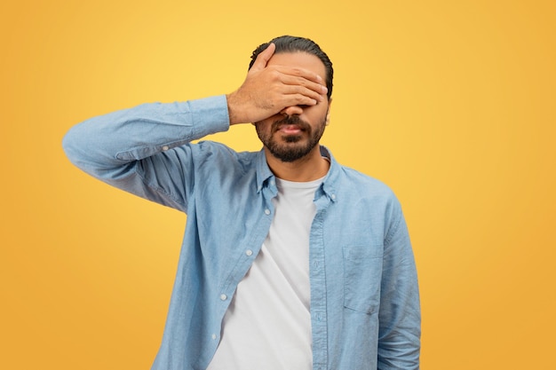 Homem cobrindo o rosto com a mão em fundo amarelo